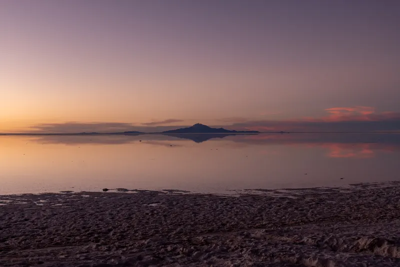 Still lake at dusk with a distant mountain mirrored in pastel water