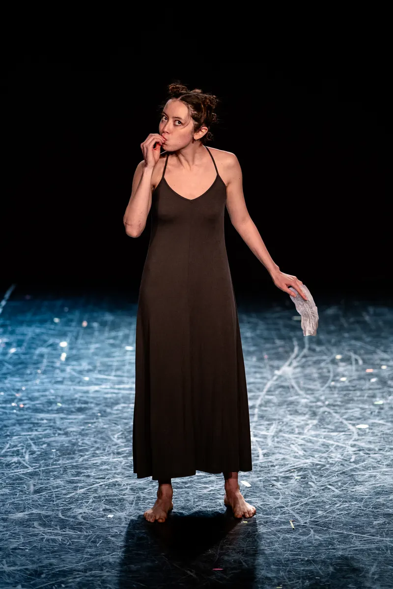 Solo performer in a long dark dress on a light-swept stage